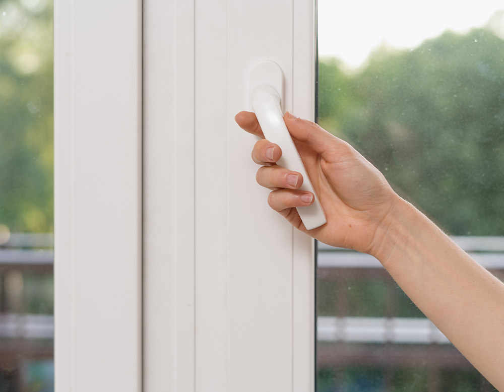 Dettaglio di una mano che apre la maniglia di una finestra in PVC bianco Agostini