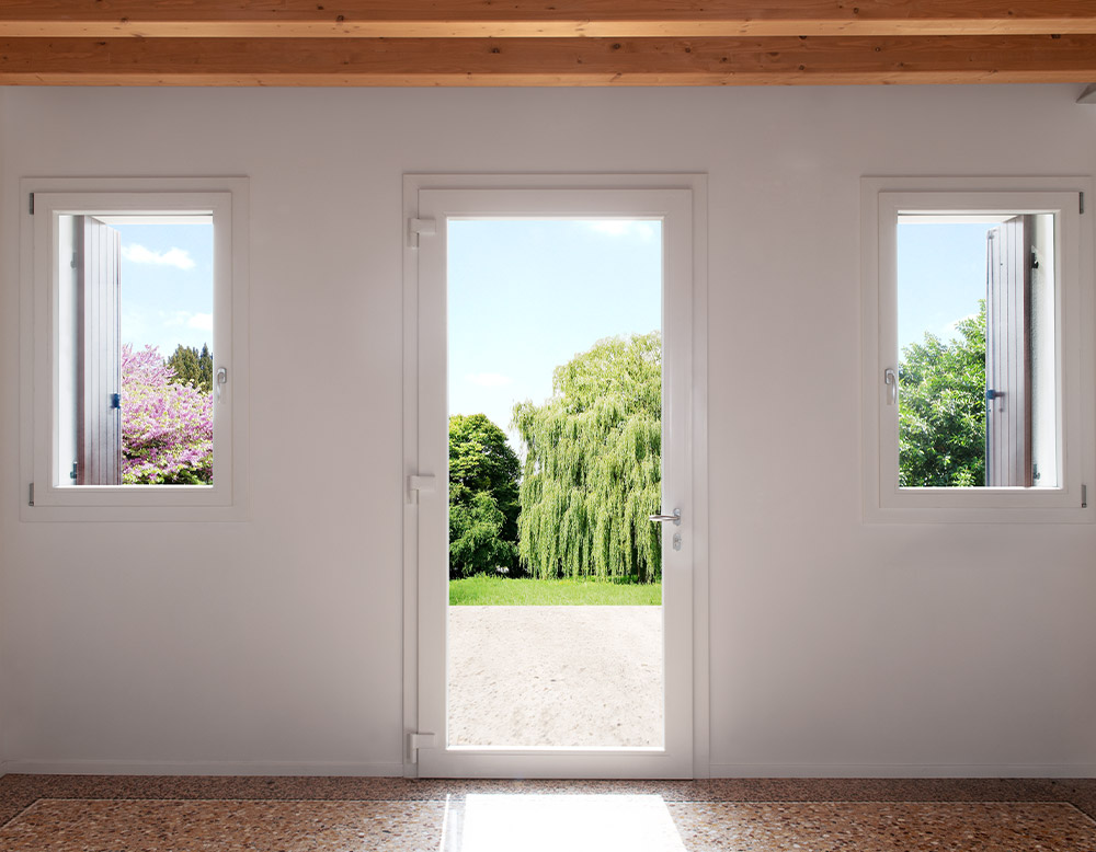 Parete con finestre e portafinestra in PVC bianco Agostini aperte verso l'interno, affacciate su un giardino