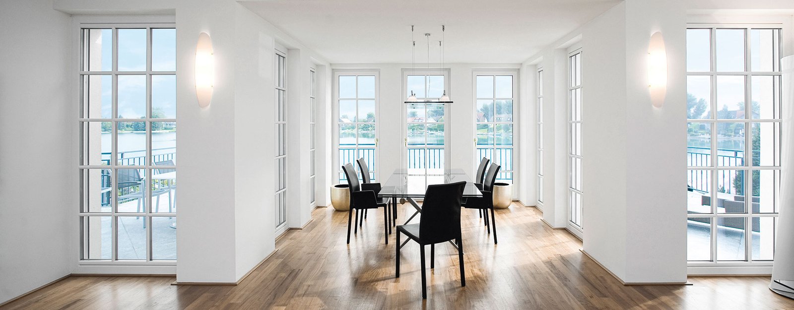Sala da pranzo luminosa con grandi finestre in PVC Internorm affacciate su un lago