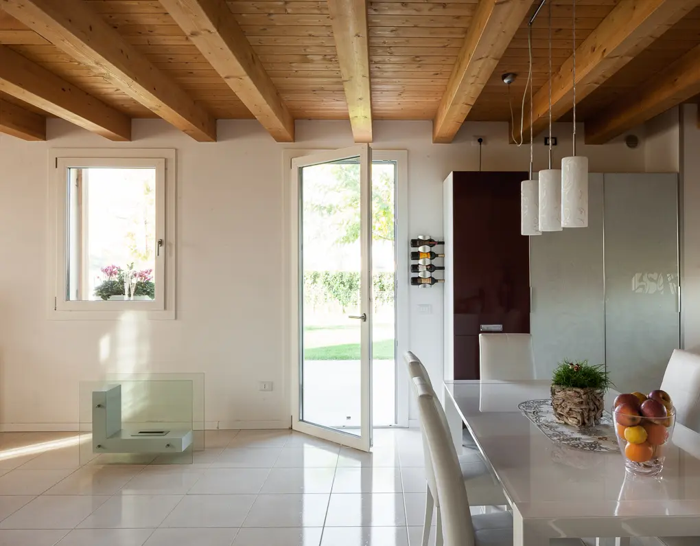 Finestra e portafinestra QFort in PVC bianco in una sala da pranzo con soffitto a travi in legno